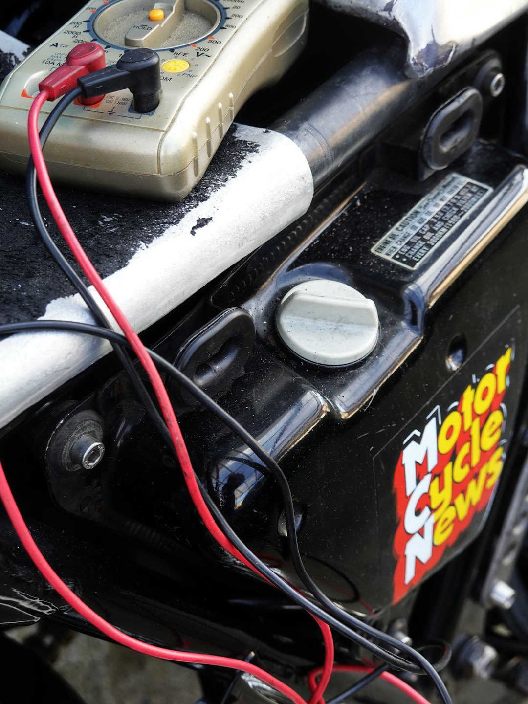 Digital multimeter testing the electrical system of a motorcycle engine.