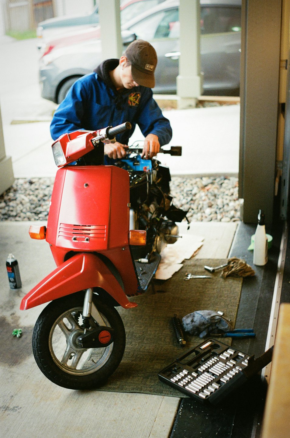 Mechanic repairs red scooter engine in a garage with tools.